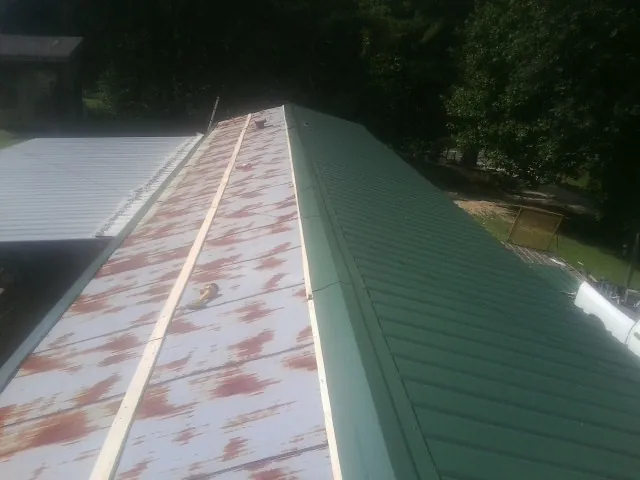 Old rusted panels beside newly installed green metal roofing — Wind Damage Roof Repair by Roofing Brothers in Benson